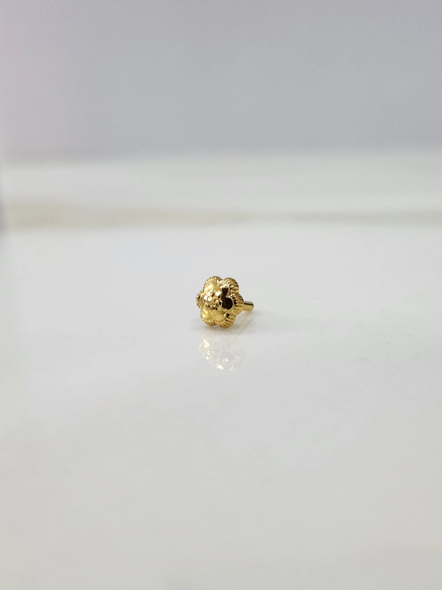 Front view of a tiny gold nose pin placed on a white background highlighting its minimal design