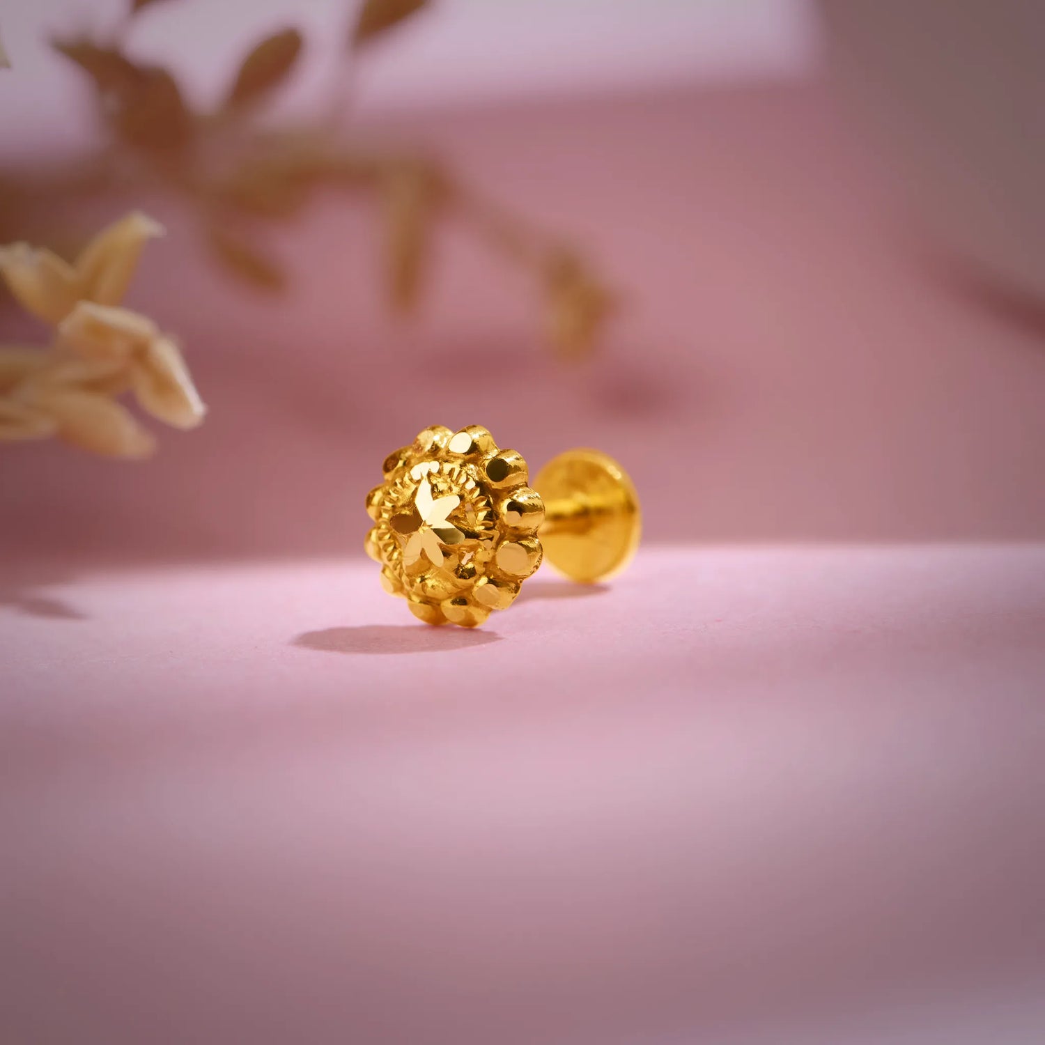 Close-up of a textured floral 18K nose pin gold placed on a soft pink background highlighting its intricate detailing