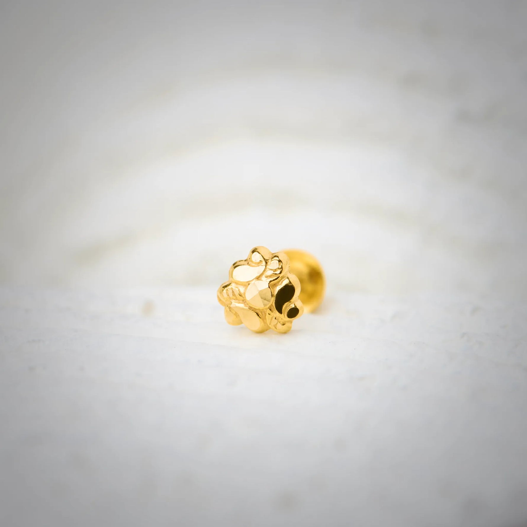 Close-up of a floral 18K nose pin gold placed on a soft white surface highlighting its intricate handcrafted detailing