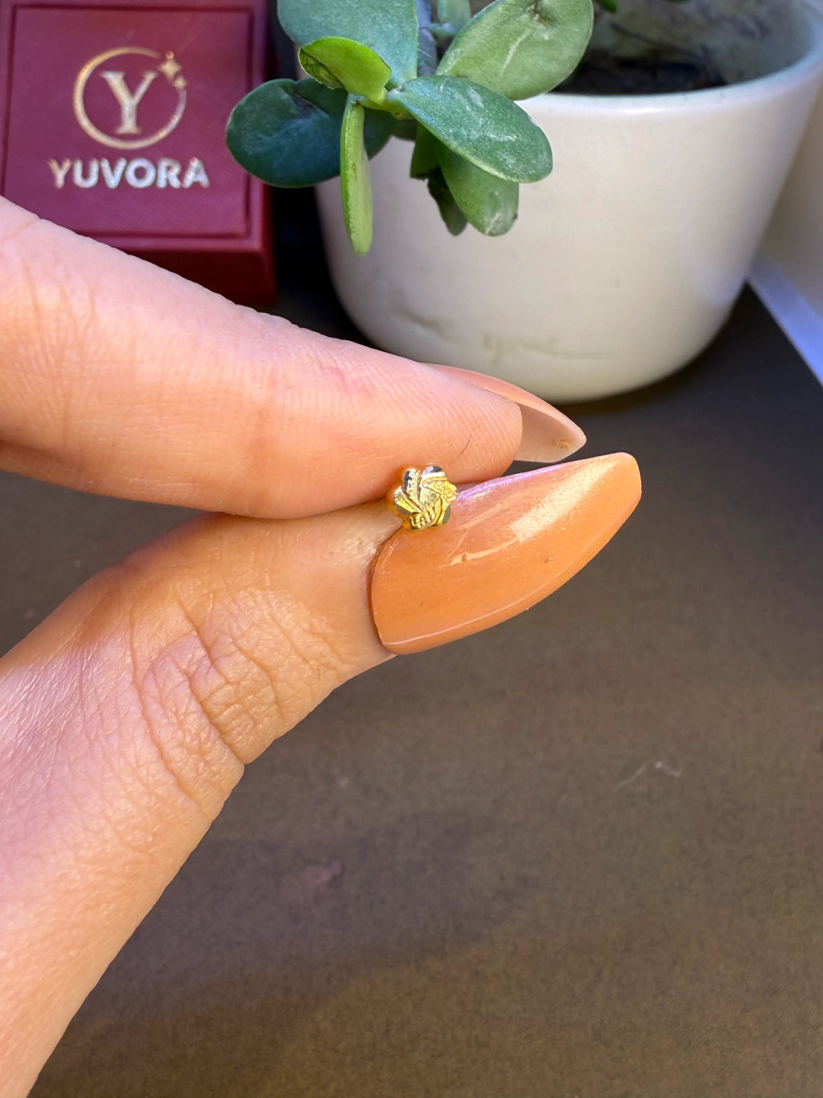 Hand view of tiny 18K nose pin gold near a Yuvora box showing its small wearable size