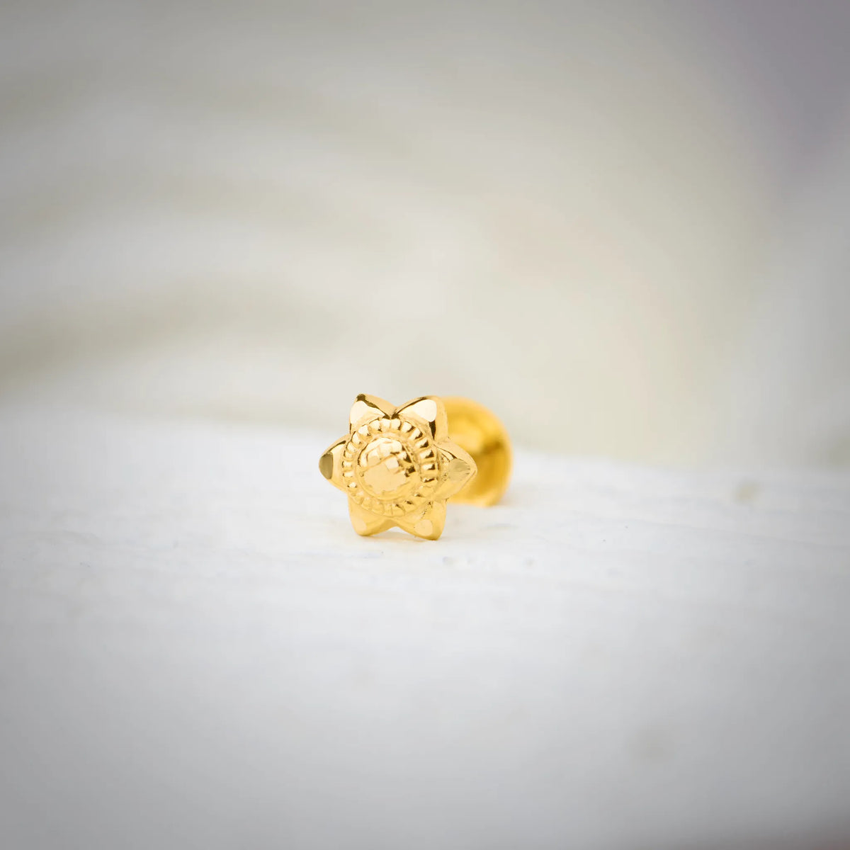 Front view of star-shaped 18K nose pin gold placed on a soft white surface highlighting its detailed floral carving