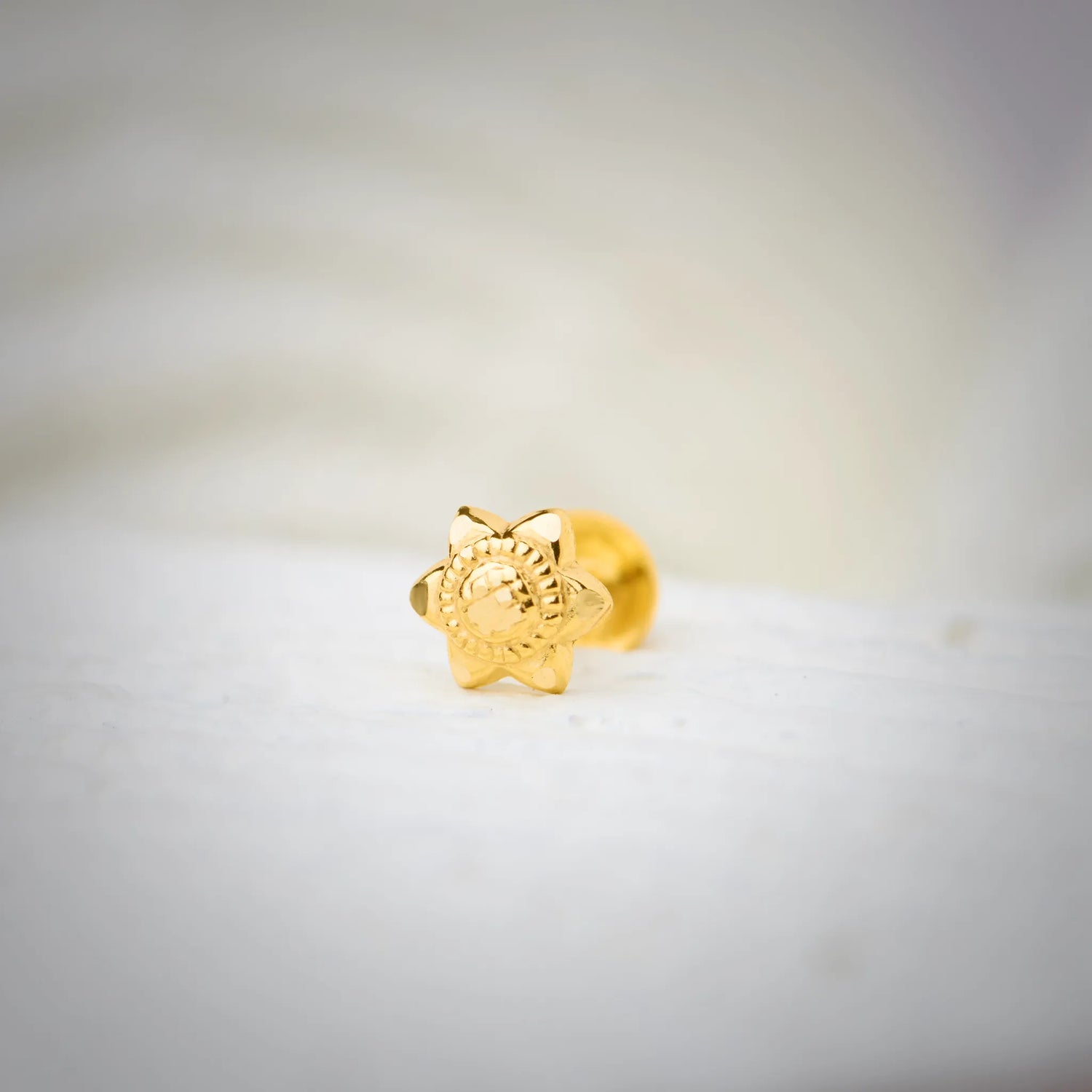 Front view of star-shaped 18K nose pin gold placed on a soft white surface highlighting its detailed floral carving