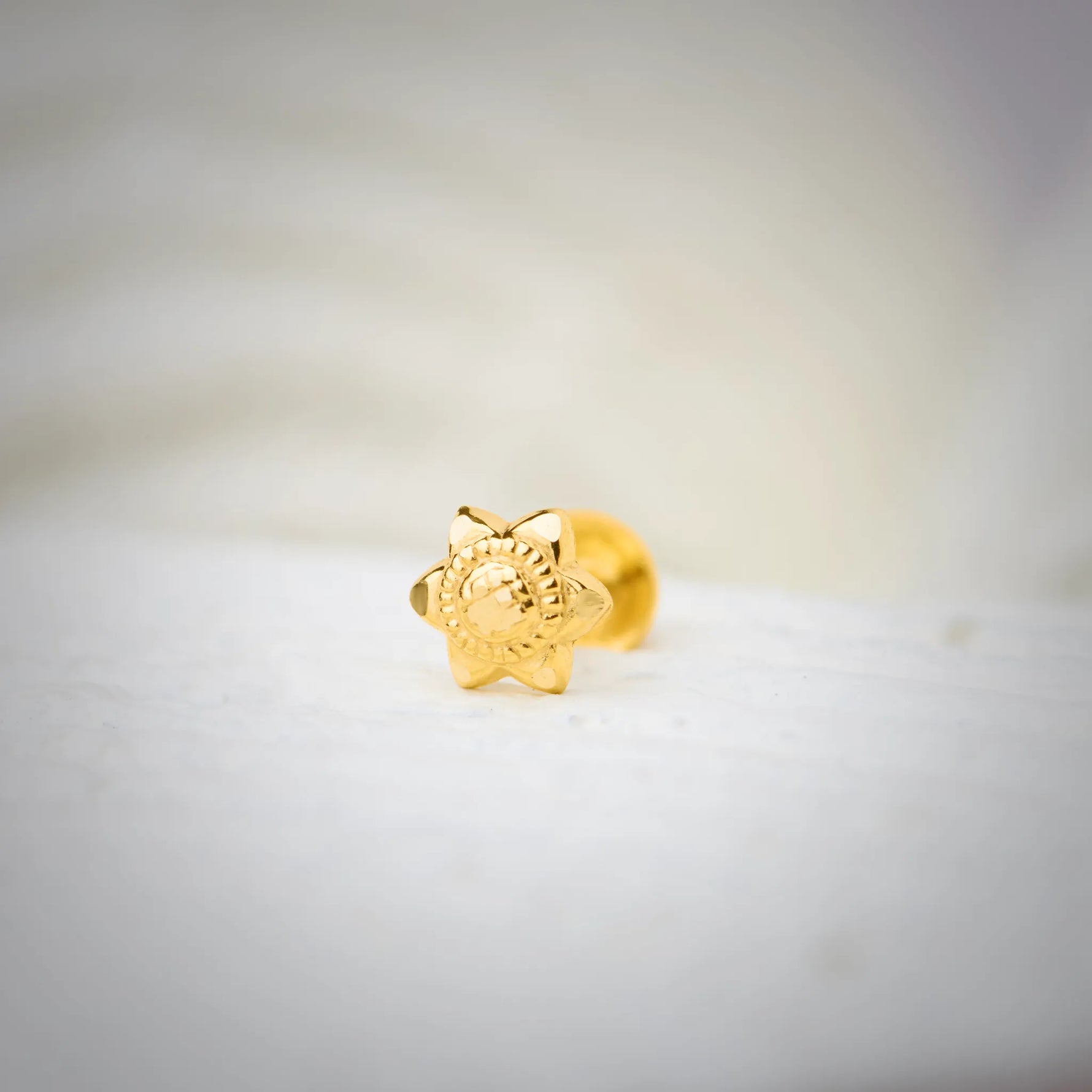 Front view of star-shaped 18K nose pin gold placed on a soft white surface highlighting its detailed floral carving