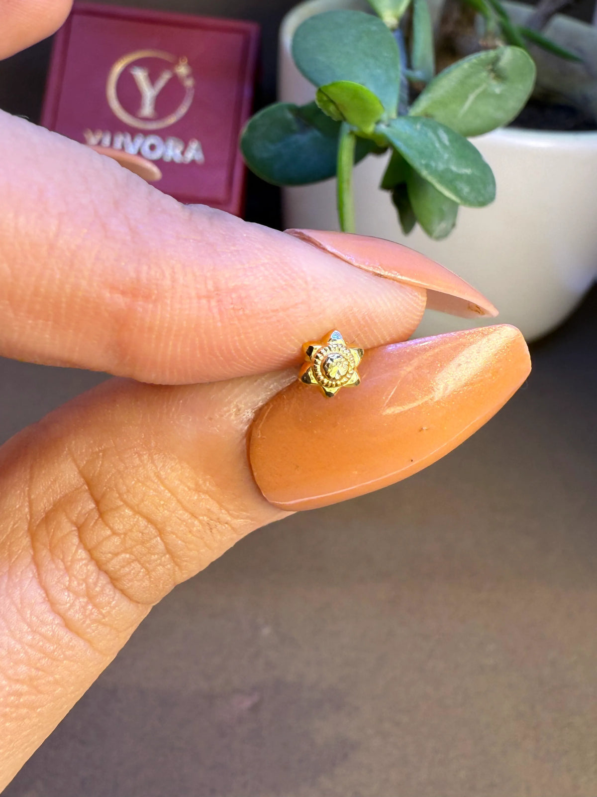 Hand view of small 18K nose pin gold held near a Yuvora box showing its tiny wearable size