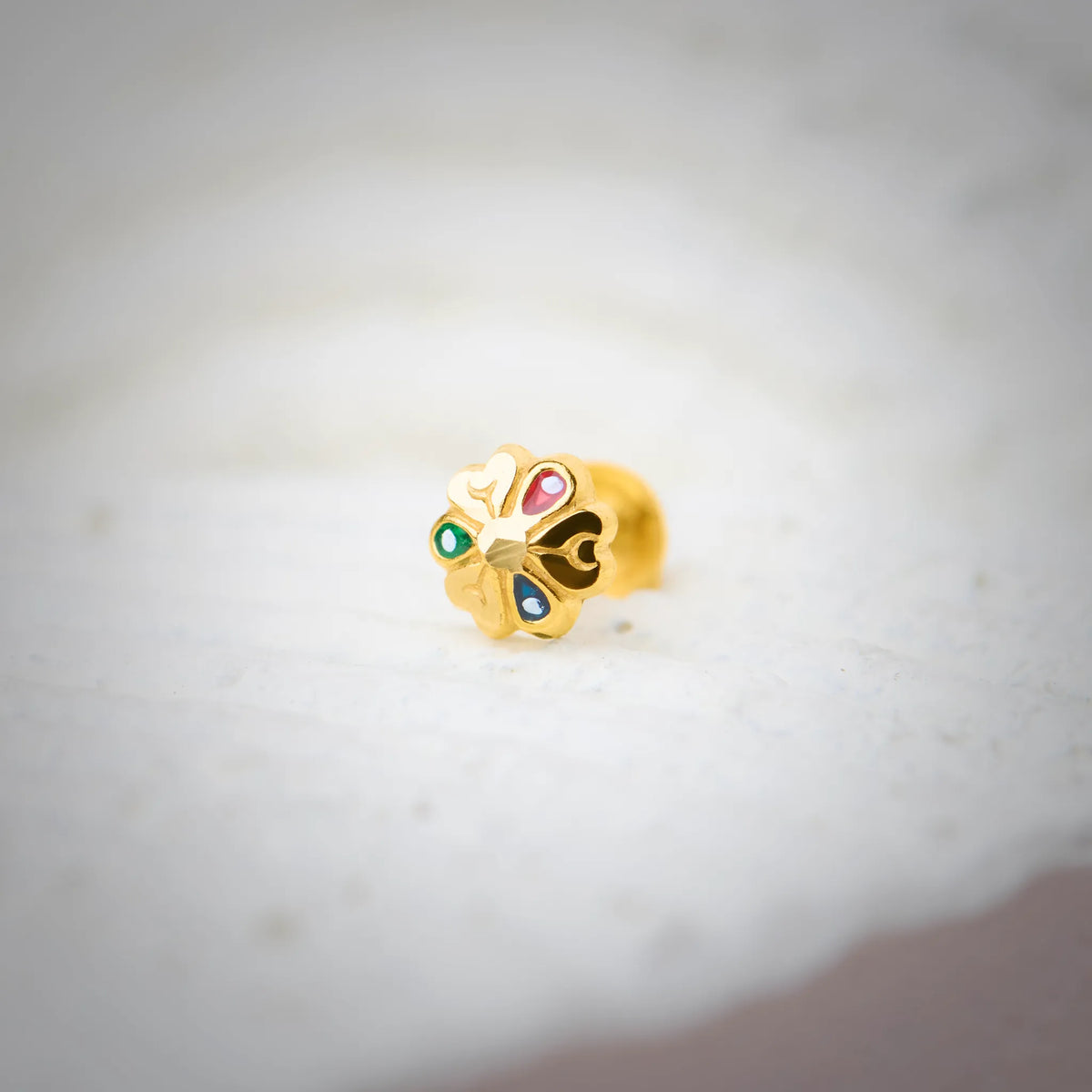 Close-up of multicolour stone 18K nose pin gold placed on a soft white surface highlighting its vibrant detailing