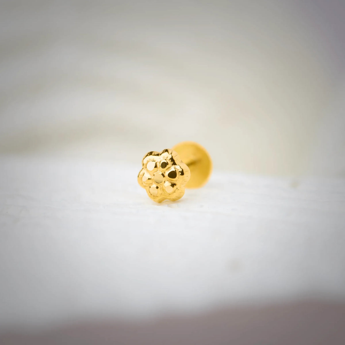 Close-up of floral textured 18K nose pin gold placed on a soft white surface highlighting its polished detailing