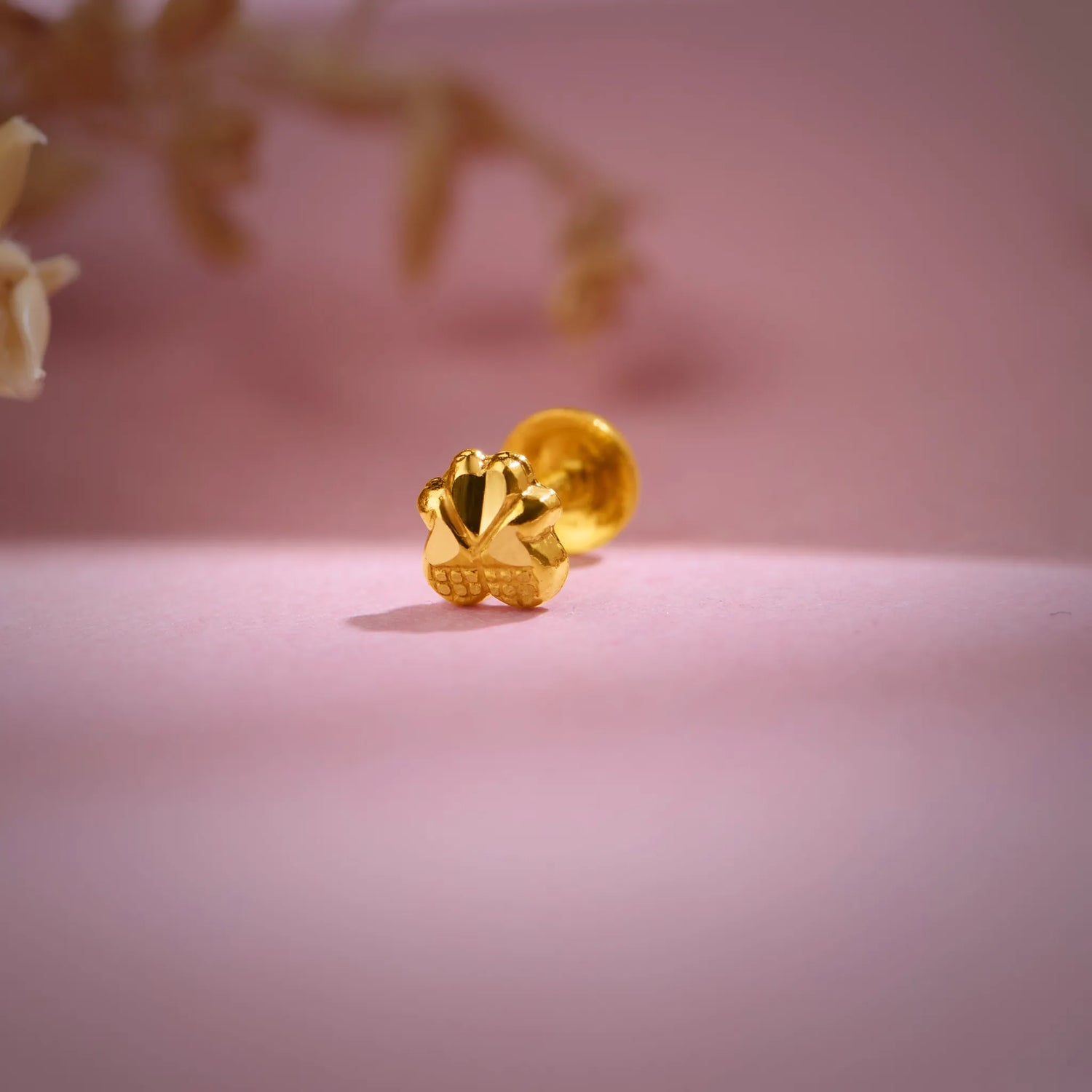 Close-up of a floral 18K nose pin gold placed on a soft pink background highlighting its polished detailing