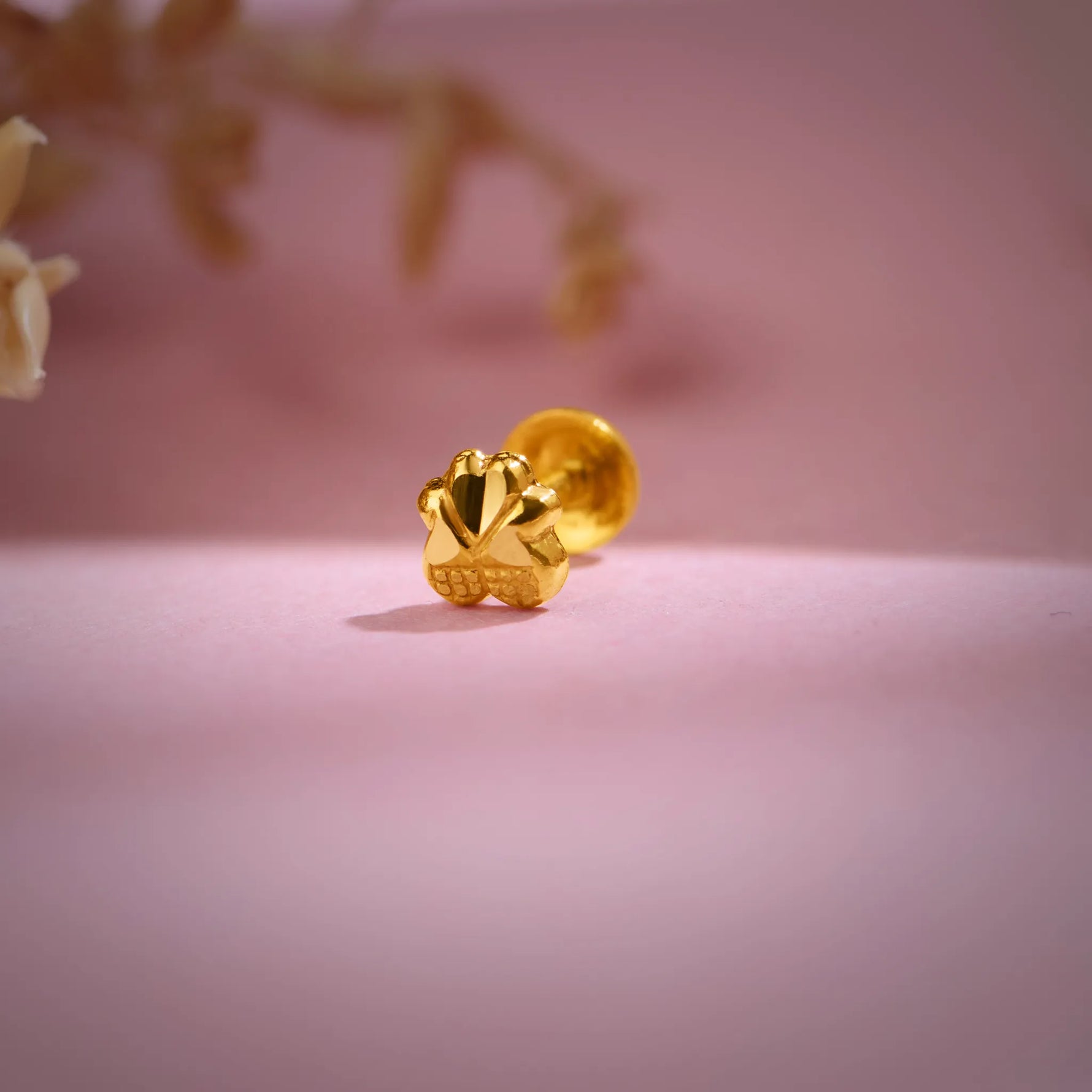 Close-up of a floral 18K nose pin gold placed on a soft pink background highlighting its polished detailing