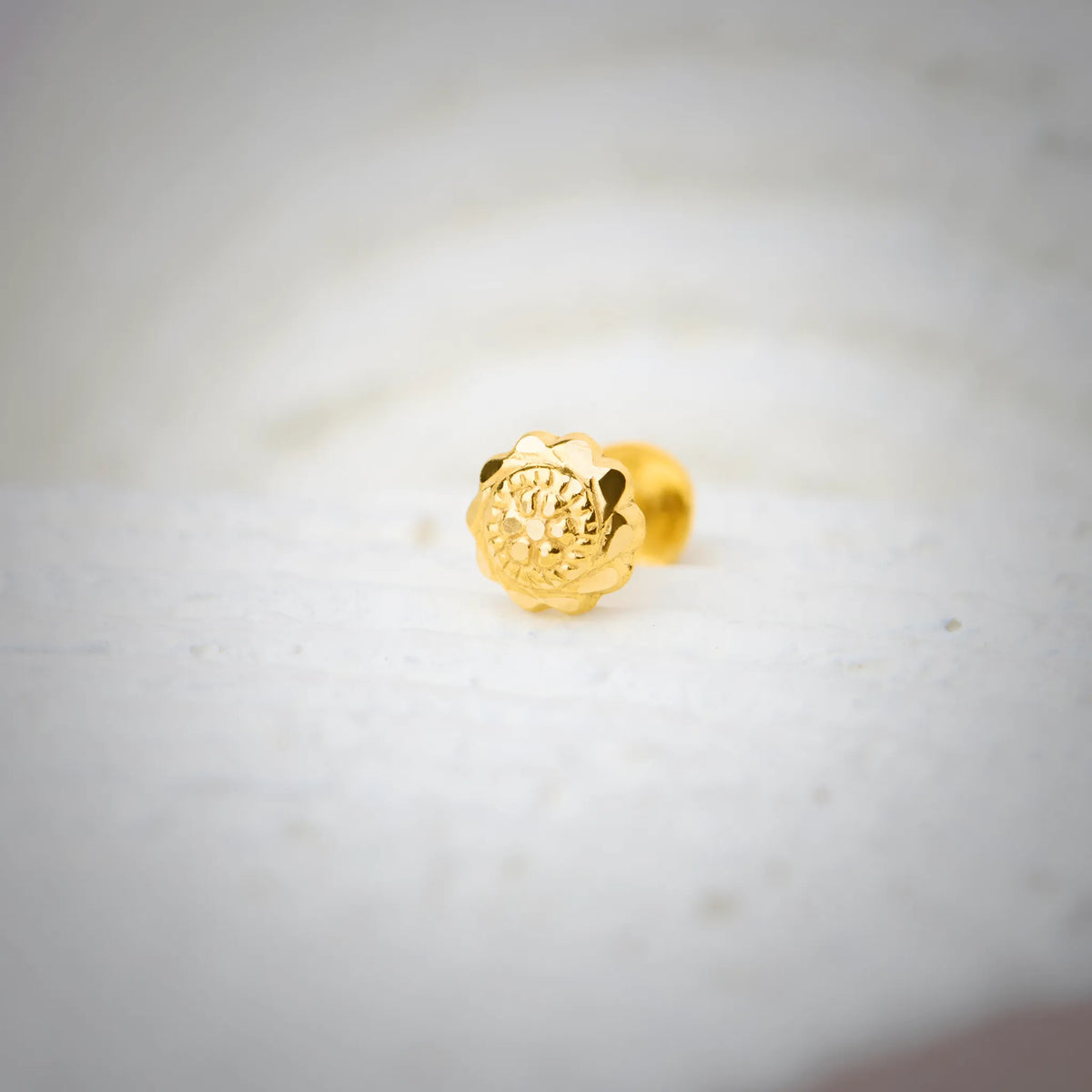 Close-up of an intricately carved 18K nose pin gold placed on a soft white surface highlighting its detailed floral design