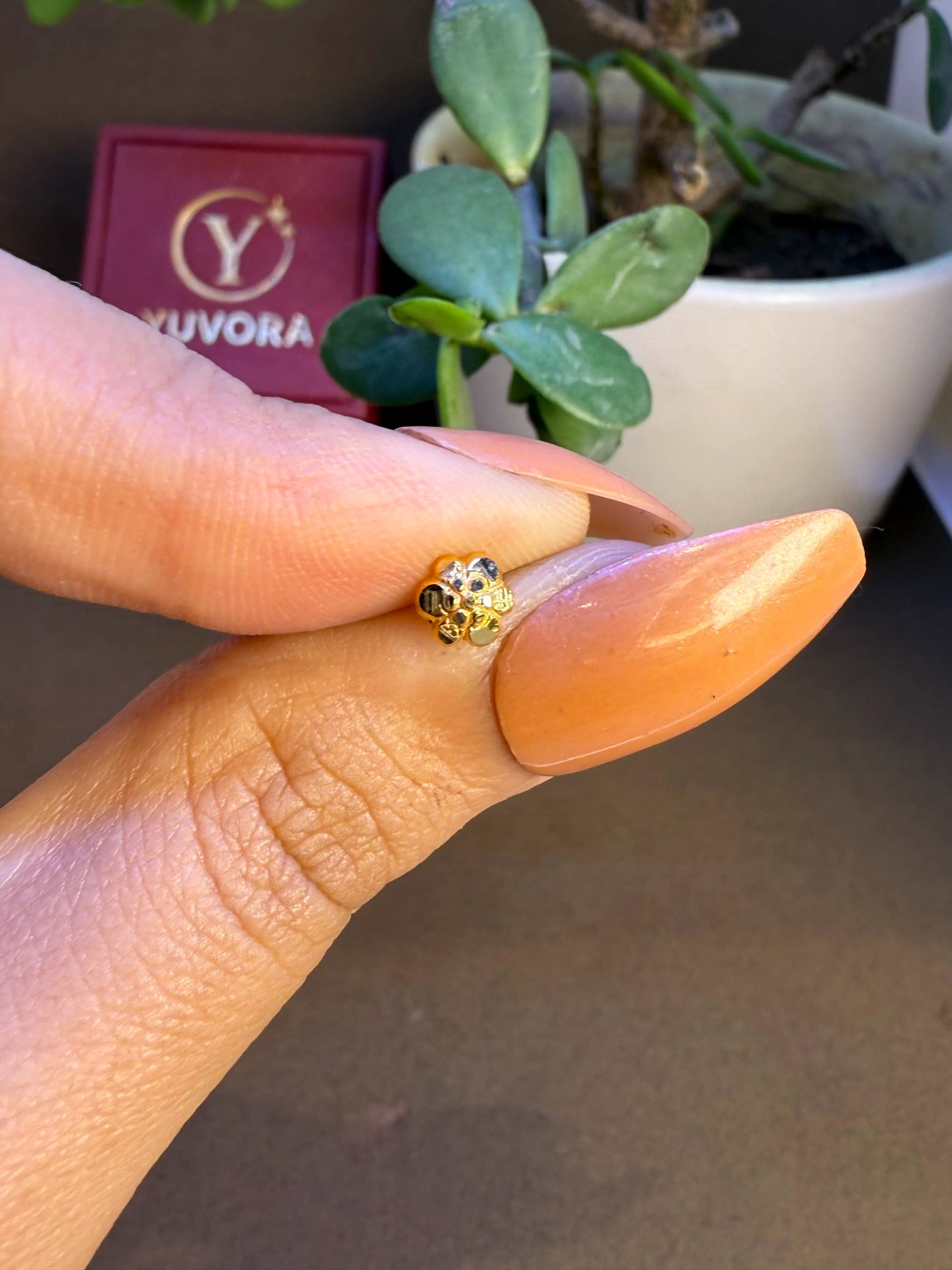 Tiny floral 18K nose pin gold held between fingers showing its miniature craftsmanship