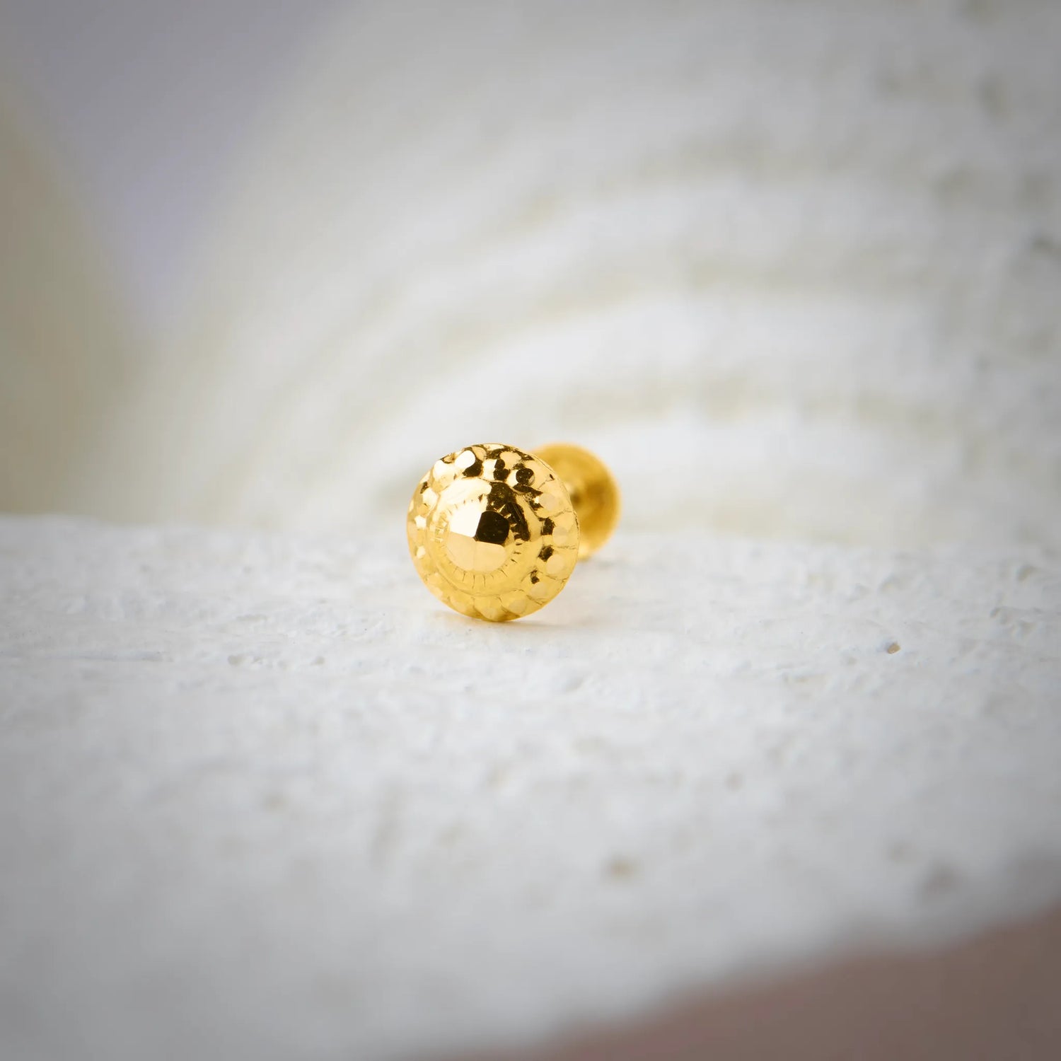 Glossy round 18K nose pin gold placed on a textured white surface highlighting its smooth polished finish