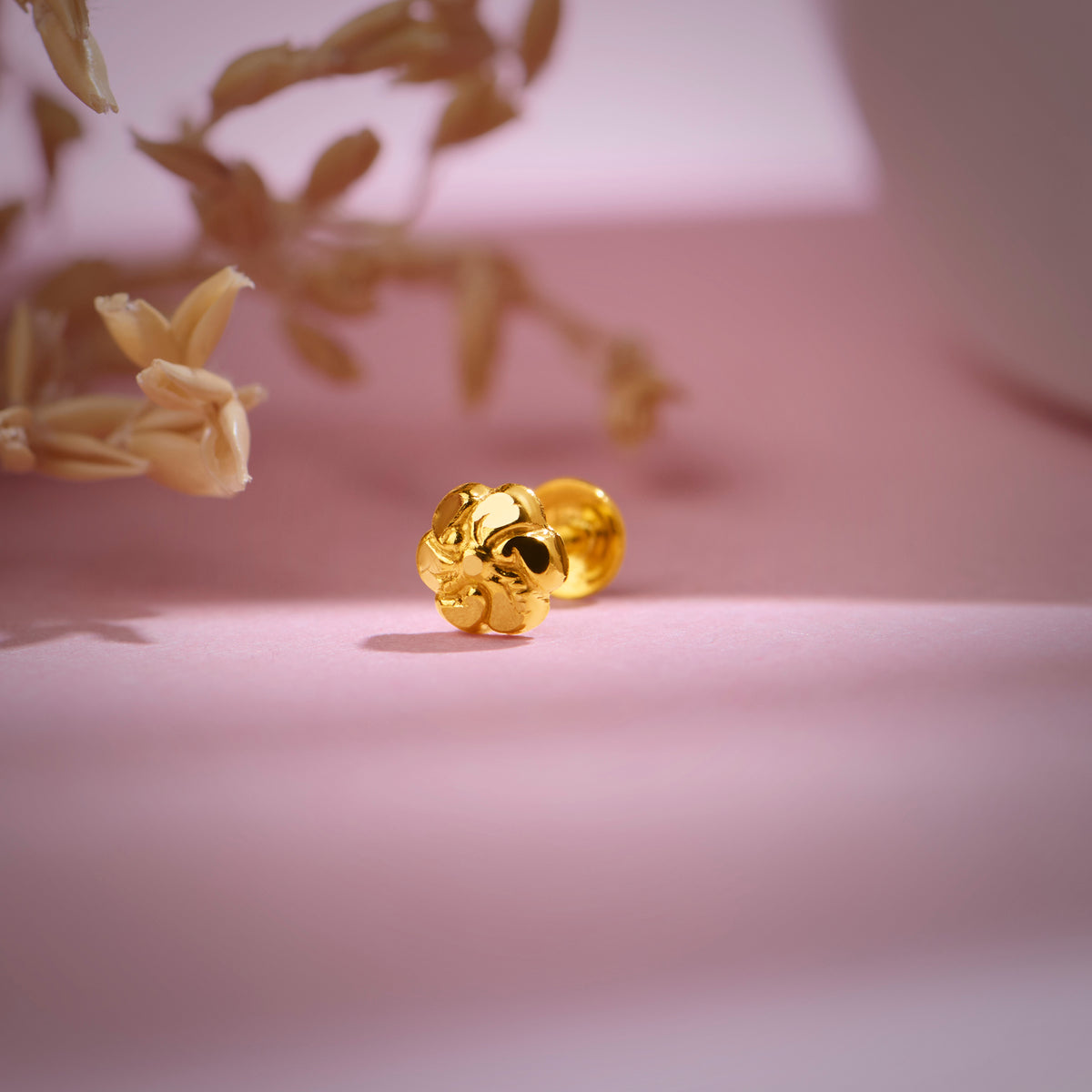 Floral 18K nose pin gold placed on a soft pink background highlighting its delicate traditional detailing
