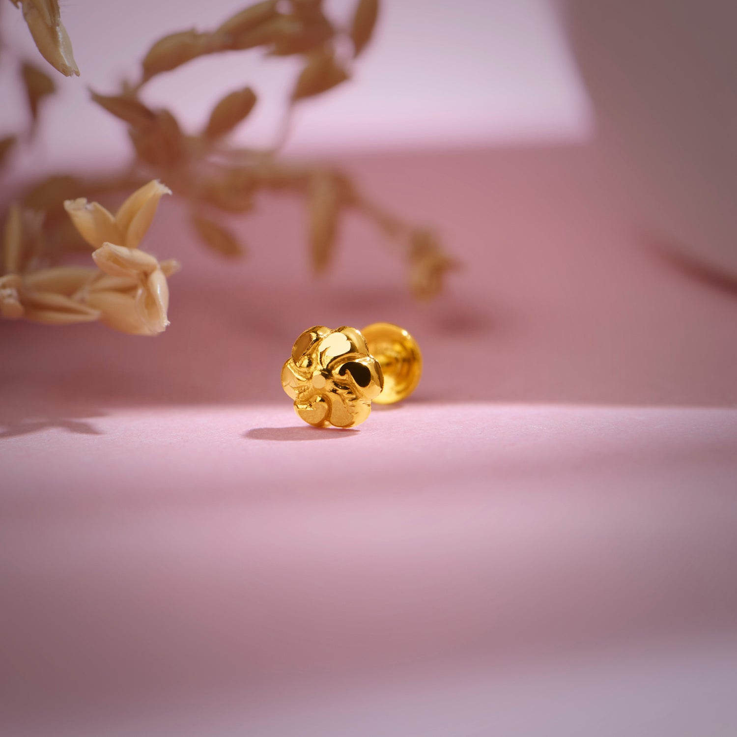 Floral 18K nose pin gold placed on a soft pink background highlighting its delicate traditional detailing