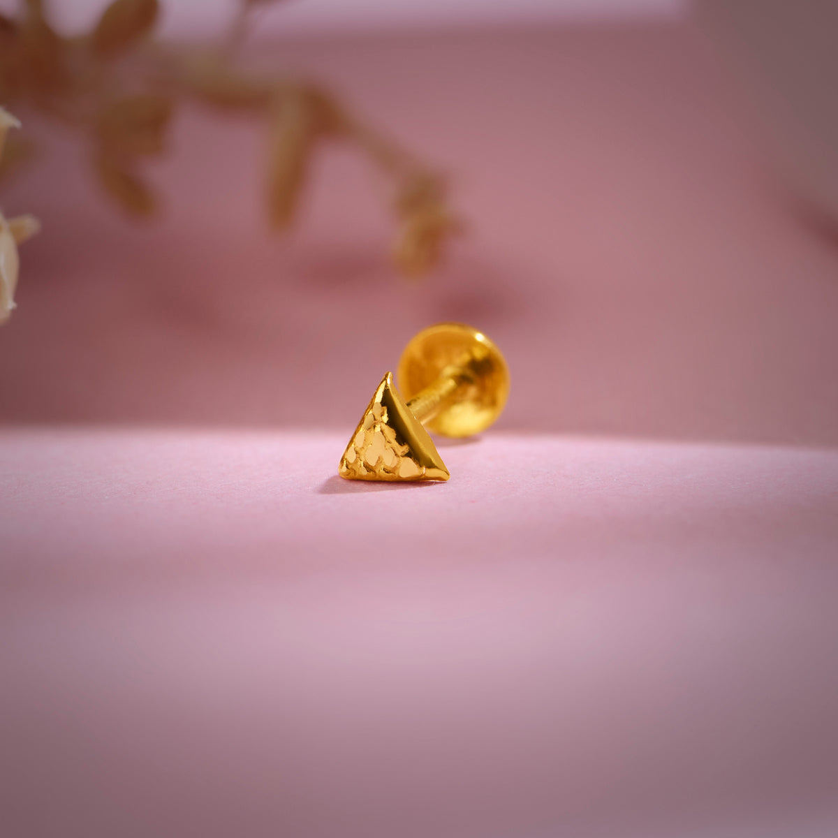 Triangle-shaped 18K nose pin gold placed on a soft pink background showing its modern minimalist design