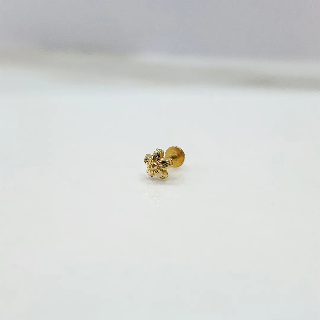 Small floral 18K nose pin gold placed on a white surface for clear visibility of the fine design
