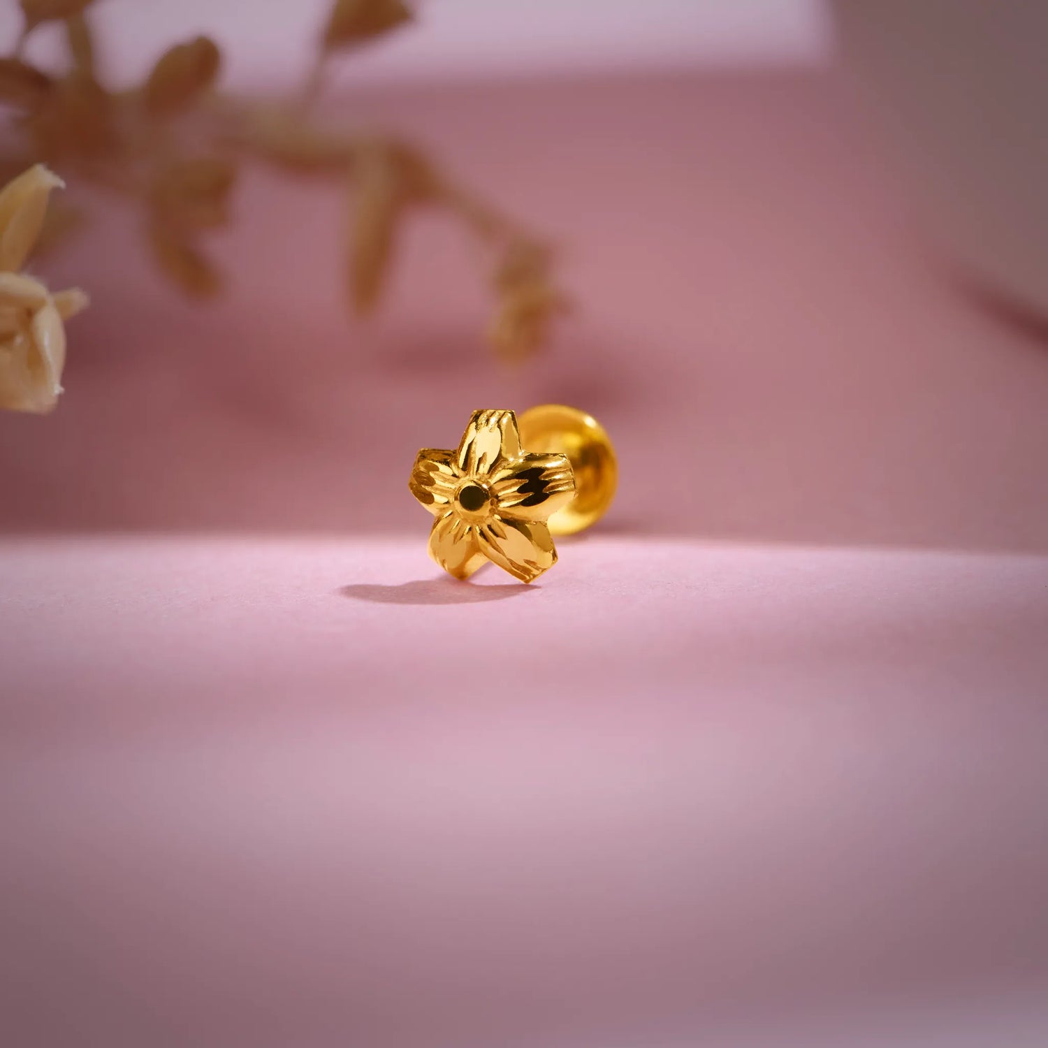 Floral 18K nose pin gold photographed on a soft pink background showcasing its elegant handcrafted detailing