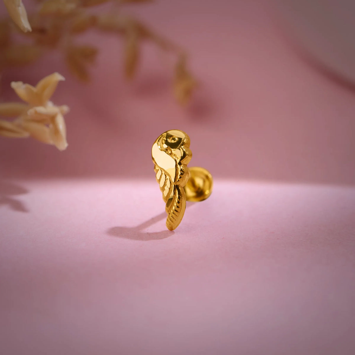 Artistic close-up of a designer 18K nose pin gold on a soft pink background