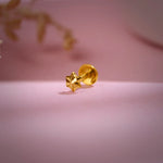 Gold star-shaped nose pin placed on a soft pink background highlighting its shine