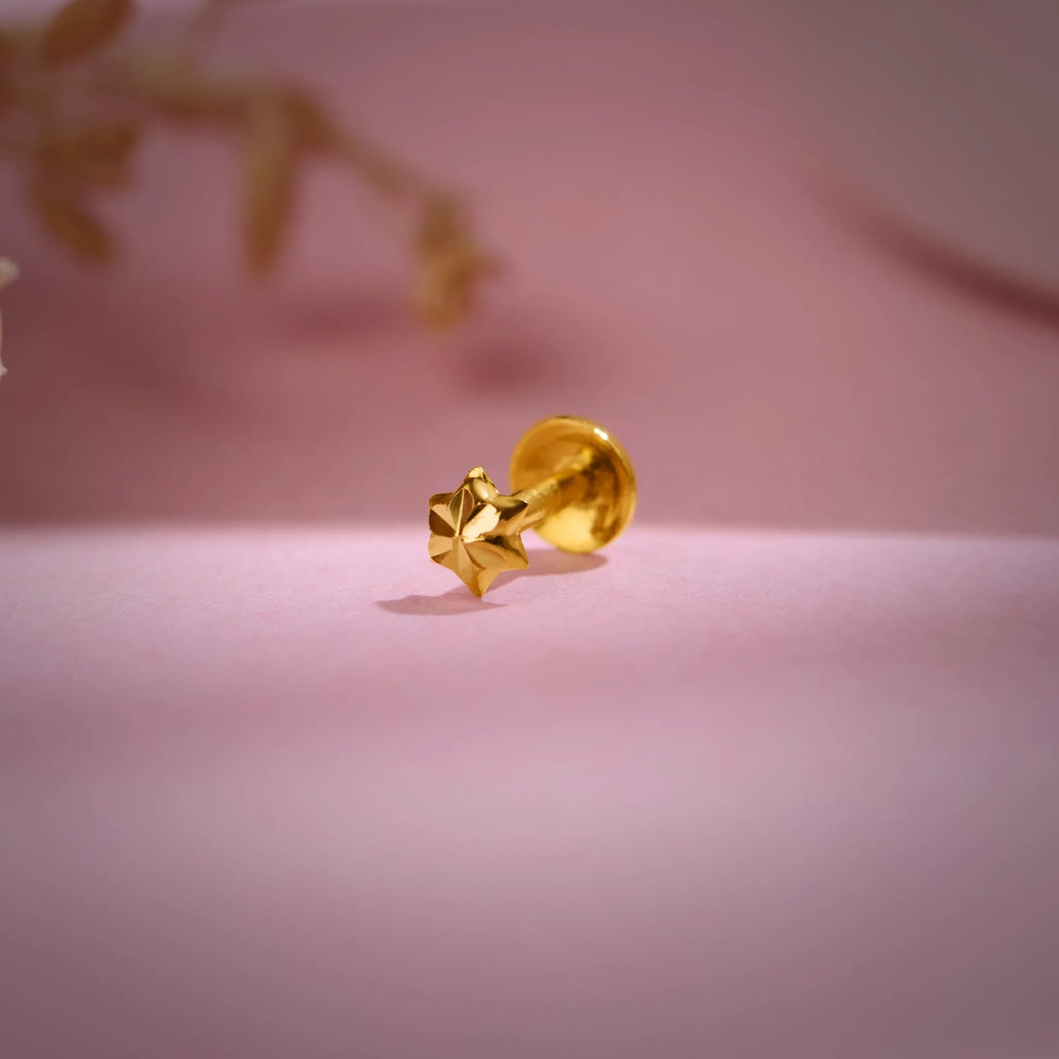Gold star-shaped nose pin placed on a soft pink background highlighting its shine