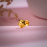 Gold nose pin placed on a soft pink background highlighting its floral detailing