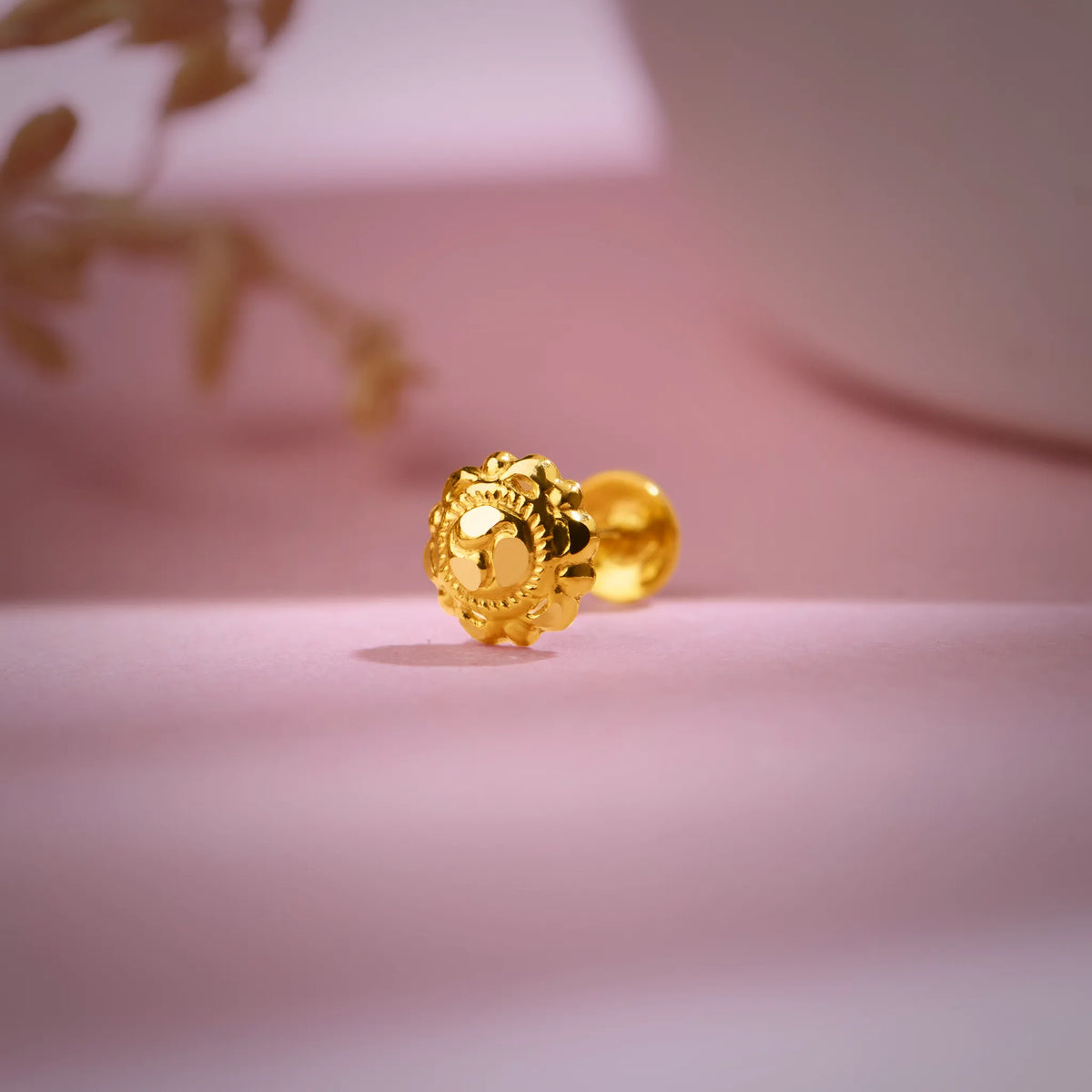 Gold nose pin placed on a soft pink background highlighting its floral detailing