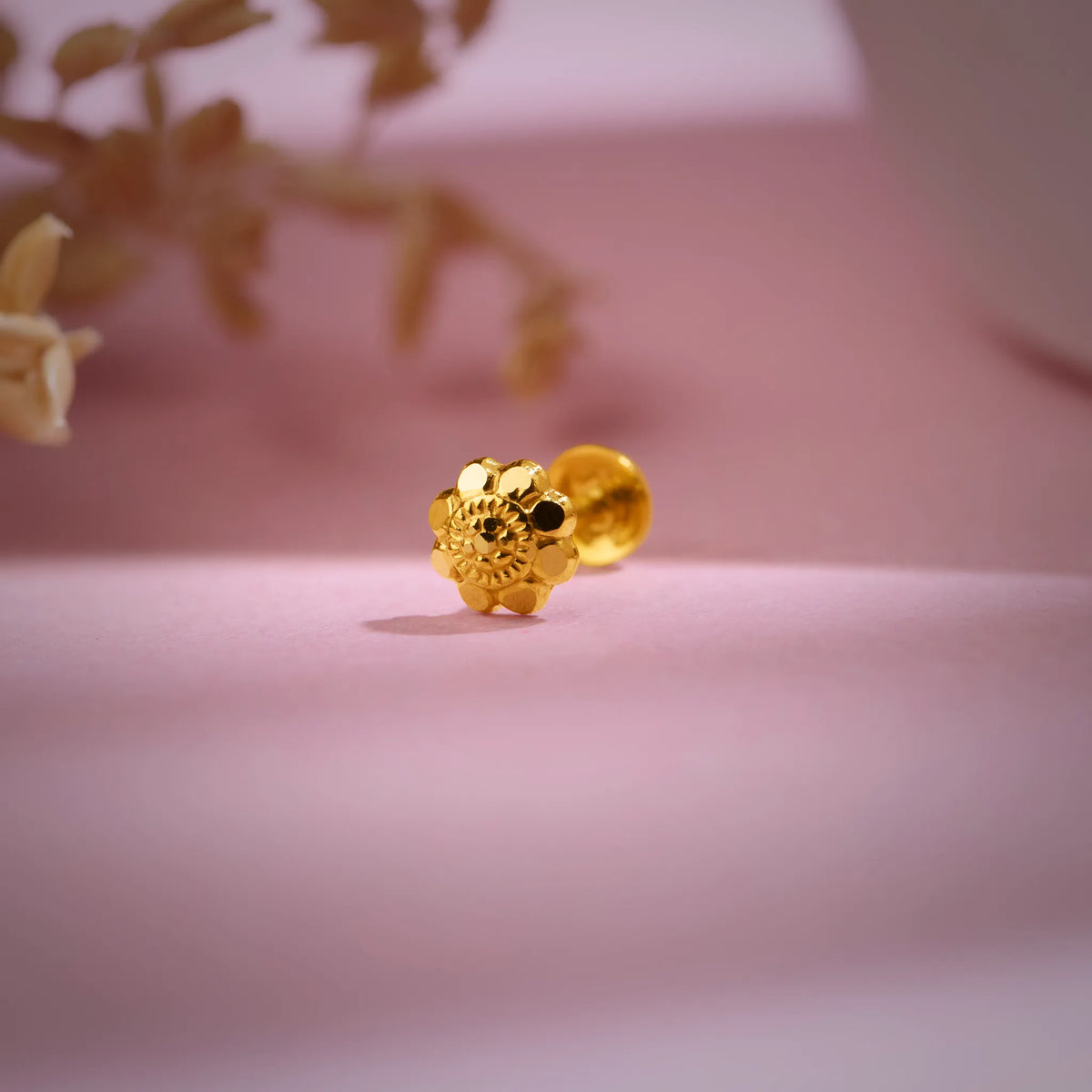 Gold nose pin placed on a soft pink background showcasing its floral detailing