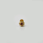 Small gold nose pin with red stone photographed on a white surface highlighting its intricate detailing