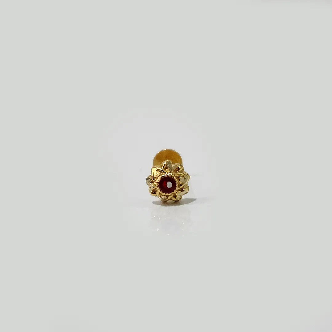 Small gold nose pin with red stone photographed on a white surface highlighting its intricate detailing