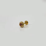 Close-up of tiny gold nose pin with a red stone placed on a white background