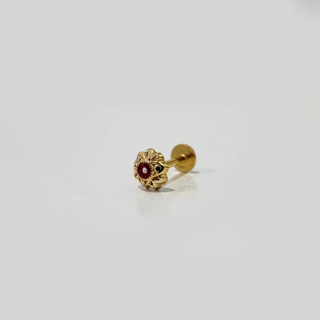 Close-up of tiny gold nose pin with a red stone placed on a white background