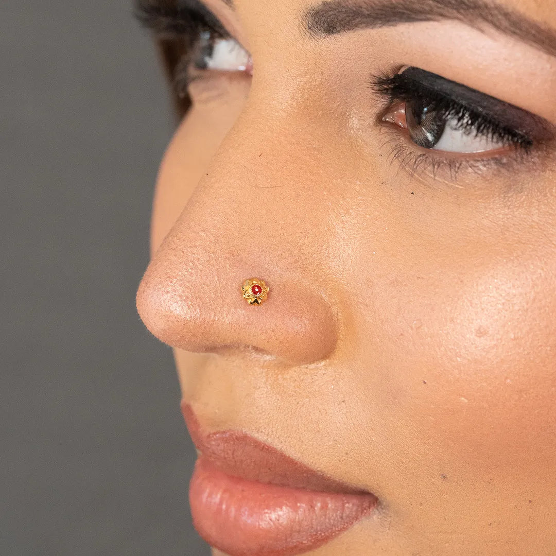 Woman wearing a small gold nose pin with a red center stone for an elegant traditional look
