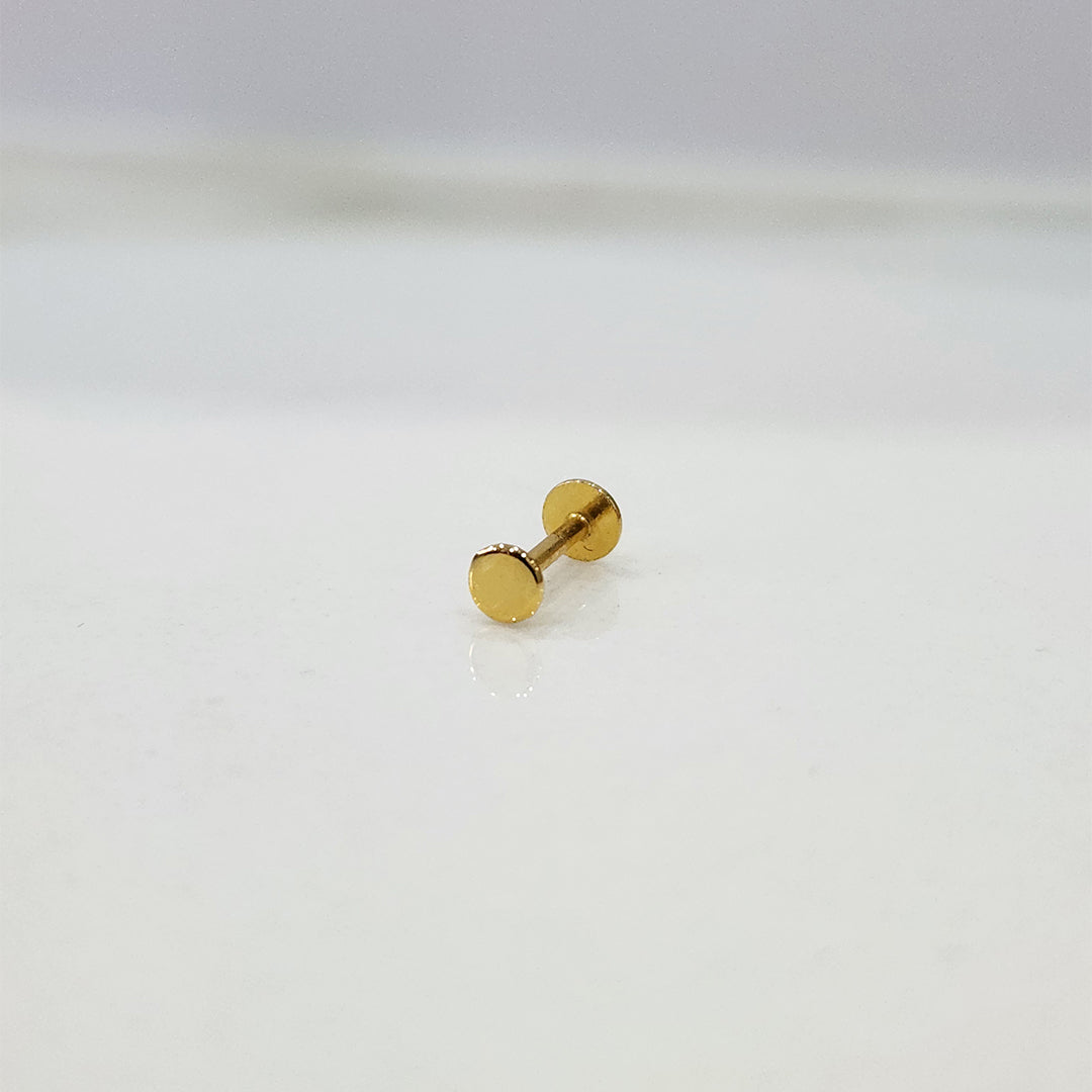 Close-up of tiny round gold nose pin placed on white surface showing clean detailing