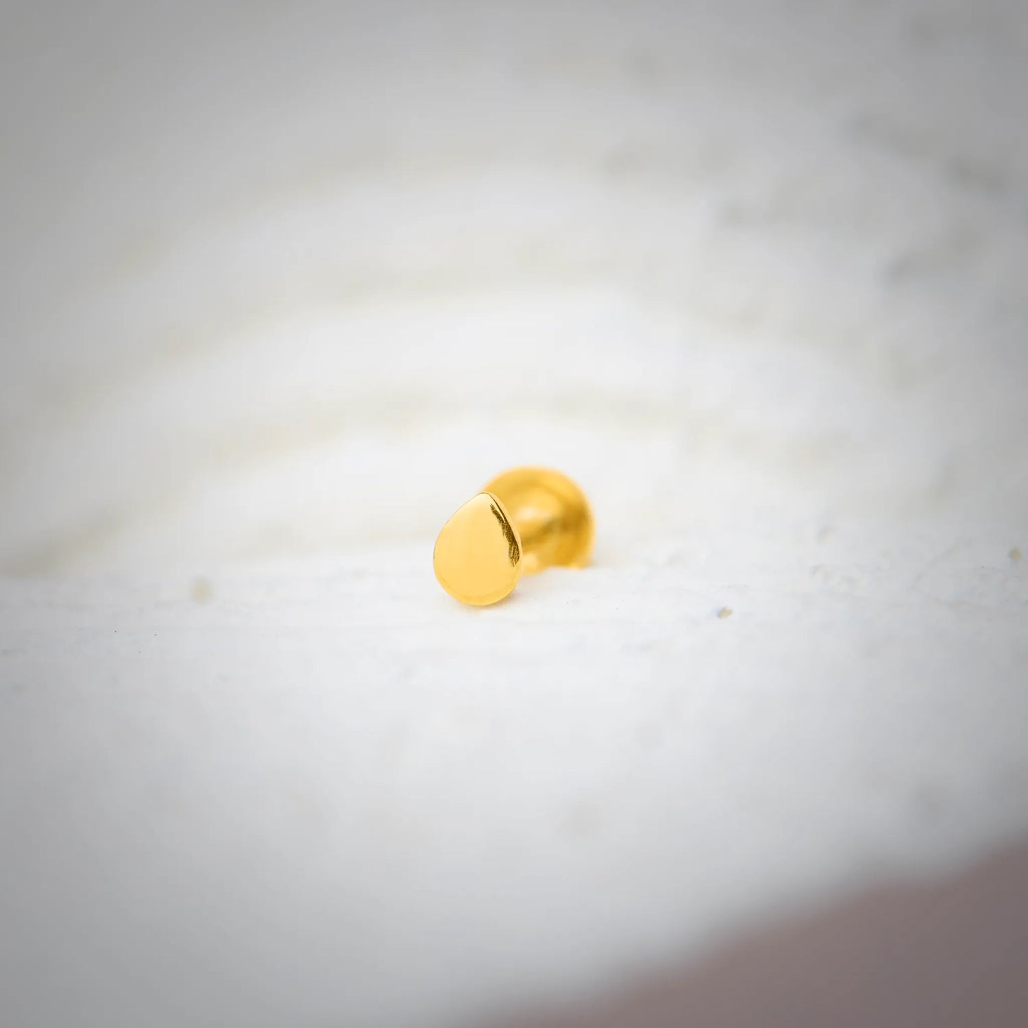 Close up view of a plain round 18K gold nose pin placed on a white textured surface showing a smooth polished finish