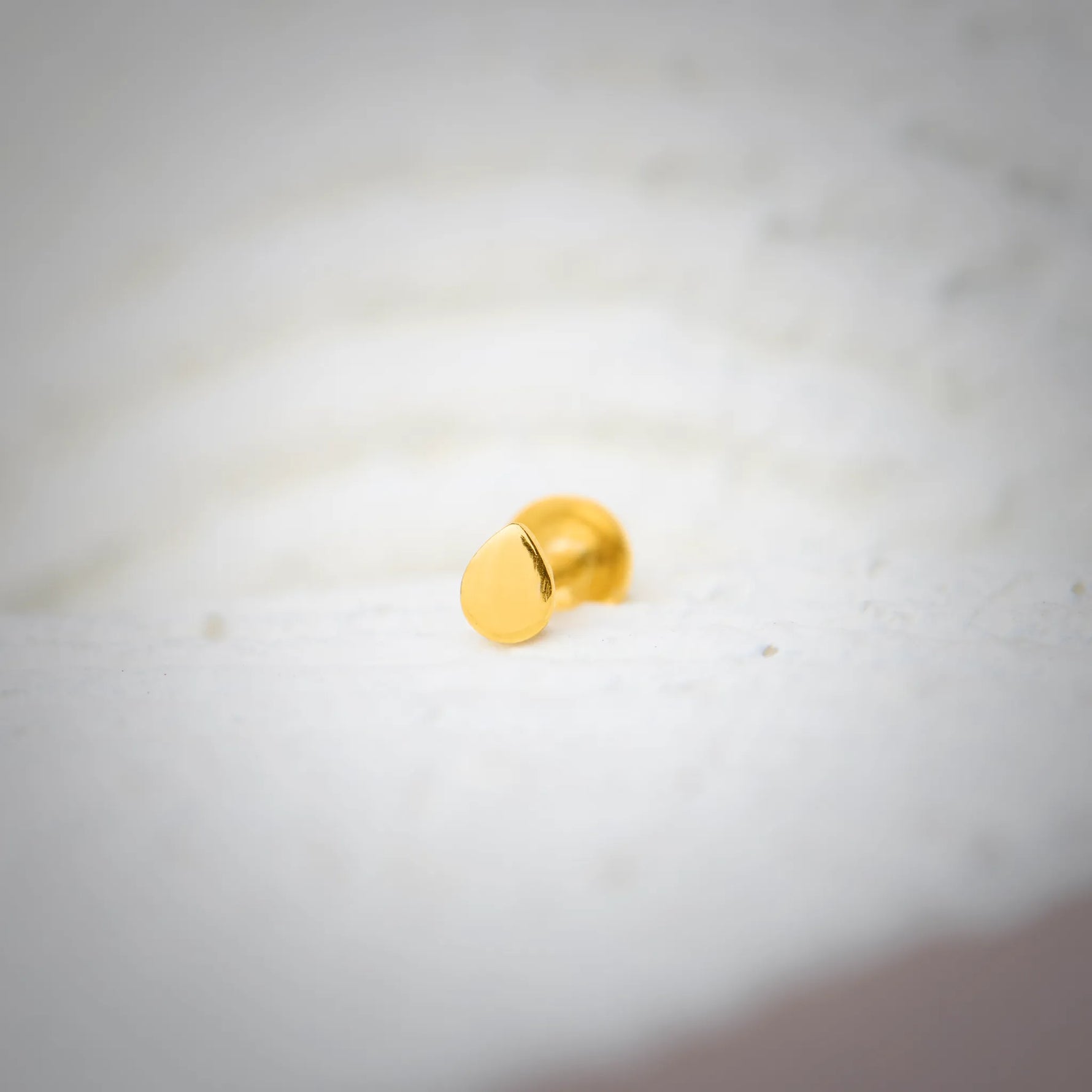 Close up view of a plain round 18K gold nose pin placed on a white textured surface showing a smooth polished finish
