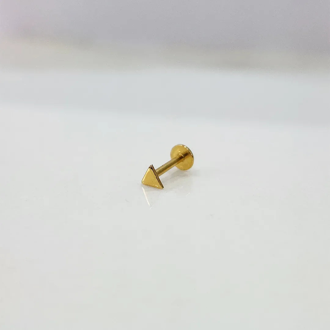 Side angle view of small triangle gold nose pin placed on white surface showing clean geometric design