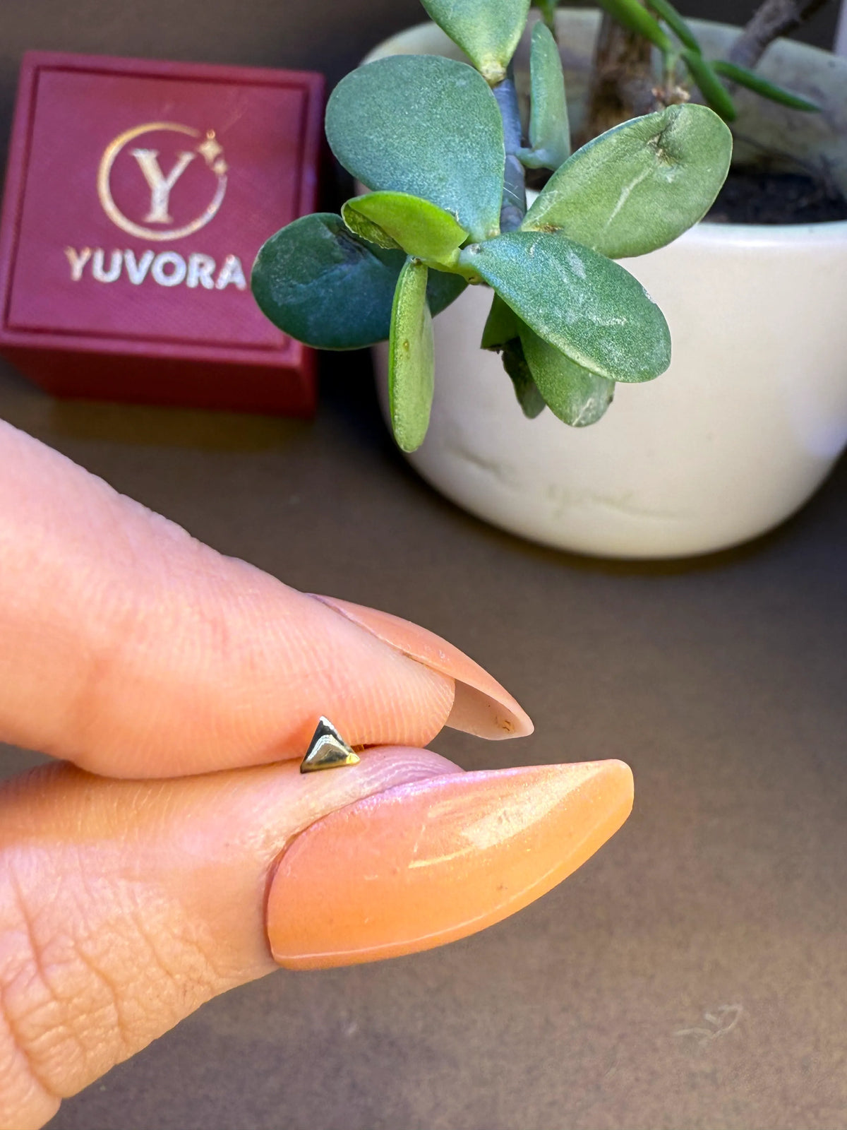 Triangle gold nose pin displayed on fingertip for real-size comparison and detailing clarity