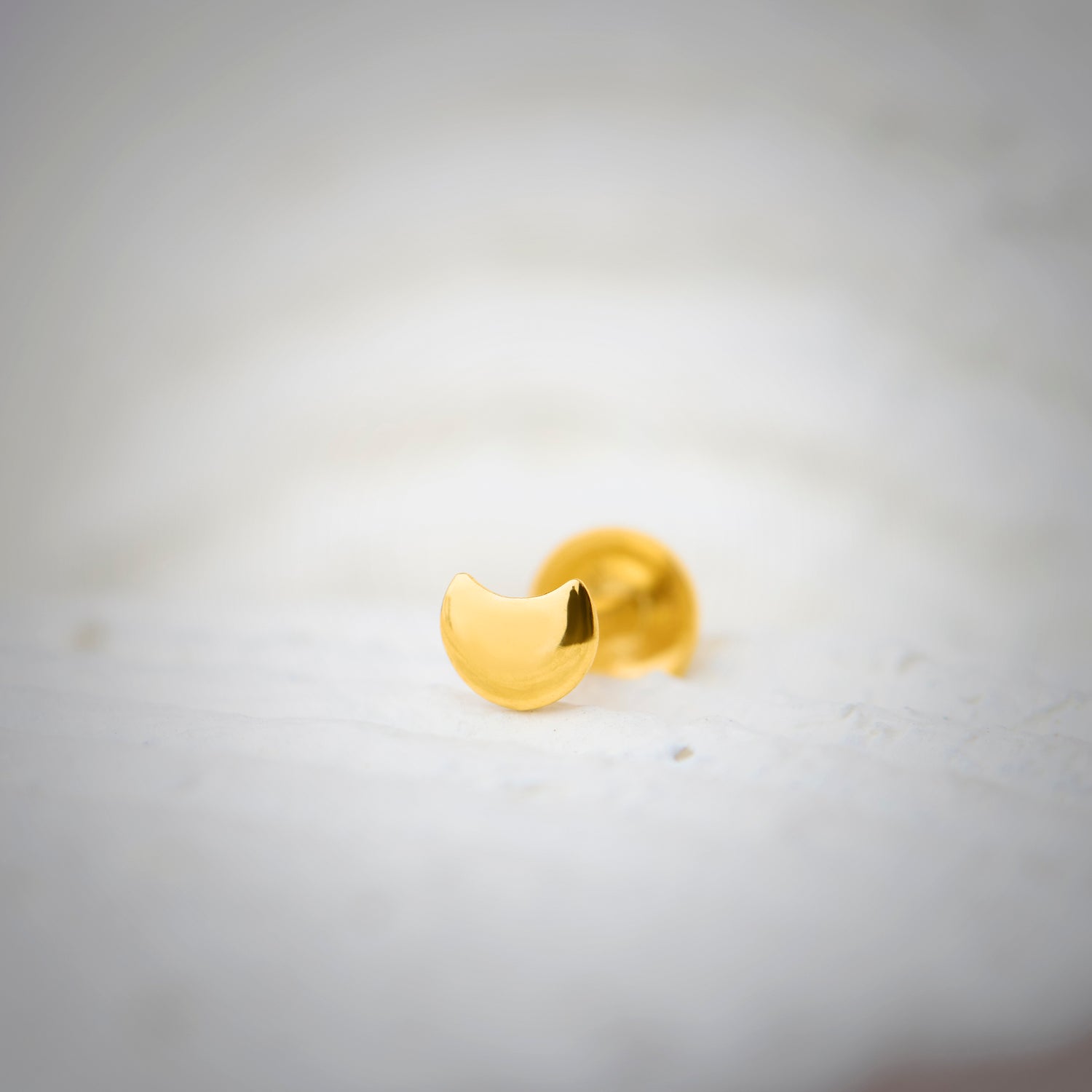 Close-up of a crescent-shaped 18K nose pin gold placed on a soft white surface highlighting its smooth polished finish