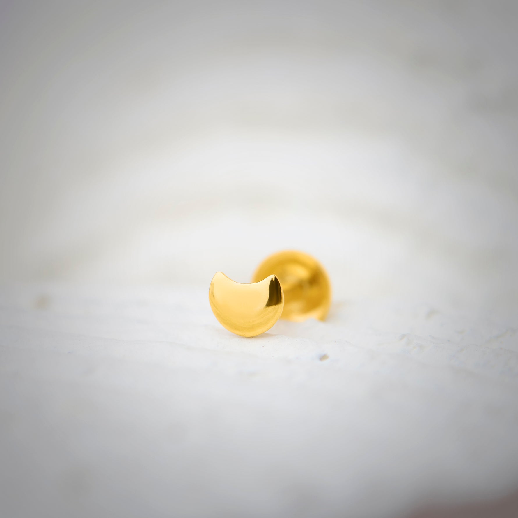 Close-up of a crescent-shaped 18K nose pin gold placed on a soft white surface highlighting its smooth polished finish