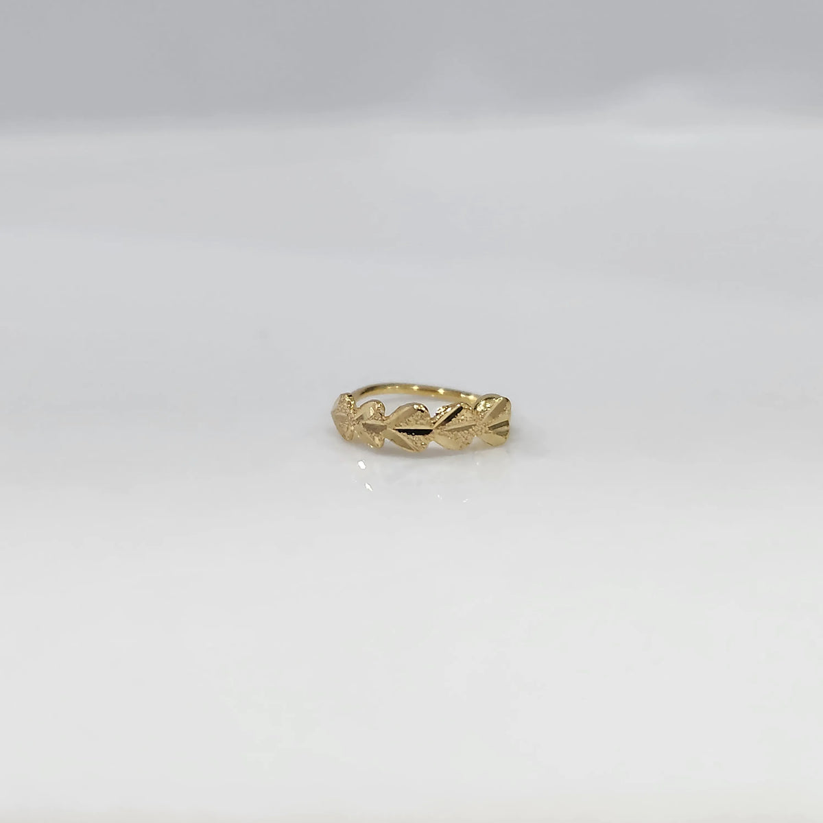 Top view of small leaf motif gold nose ring placed flat on a white surface showing its compact size