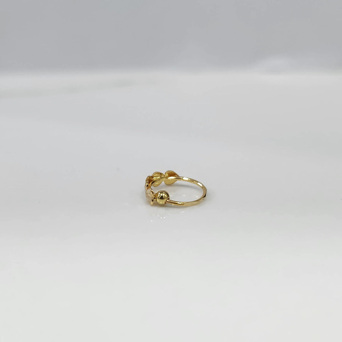 Side angle flat lay of leaf design gold nose ring on a white background emphasizing the open hoop structure