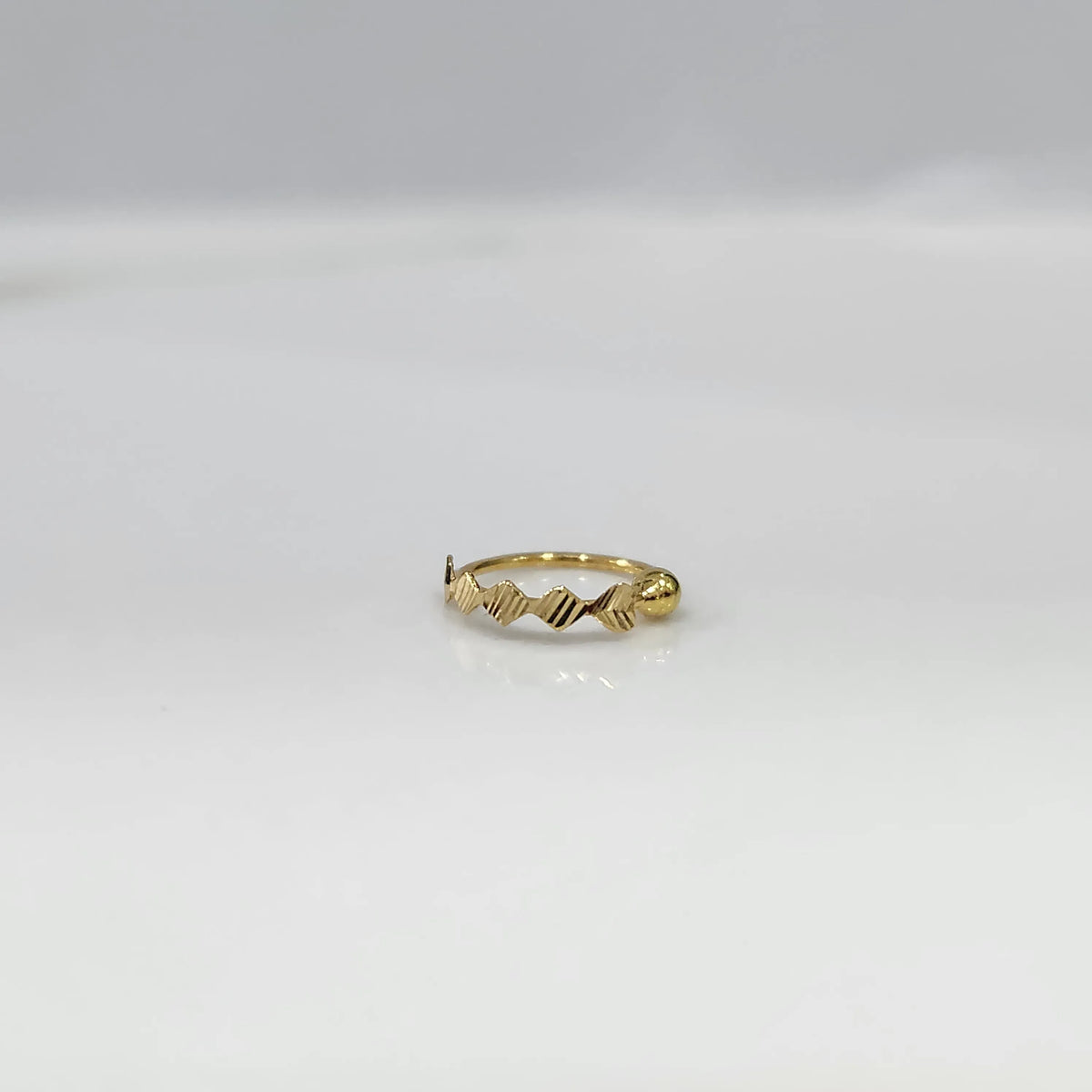 Top view of petite zigzag 18K gold nose ring laid flat on a white surface emphasizing its small size