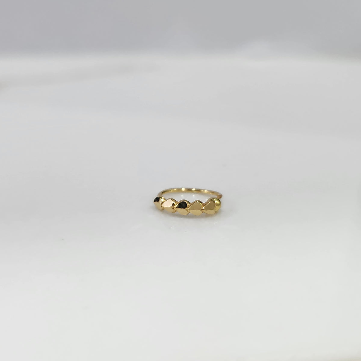 Top view of small 18K gold nose ring resting on a light grey surface showing its compact round form