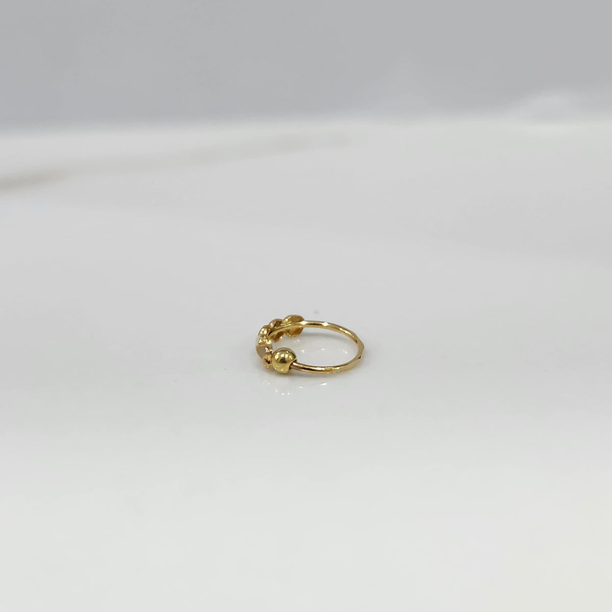 Angled close up of delicate 18K gold nose ring on a light grey background emphasizing its slim profile