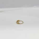 Angled close up of delicate 18K gold nose ring on a light grey background emphasizing its slim profile