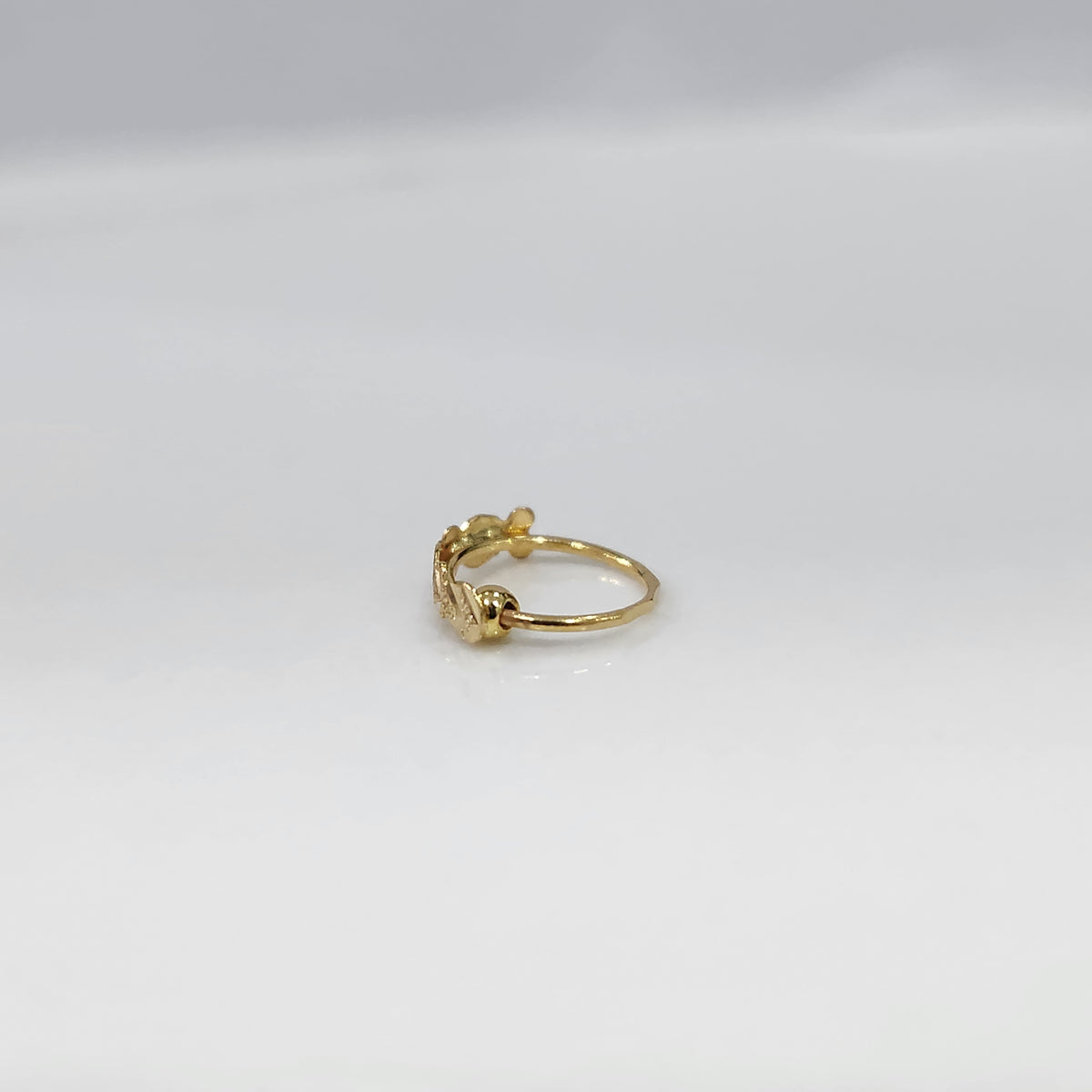 Side angle view of delicate twisted 18K gold nose ring on a white background showing slim profile