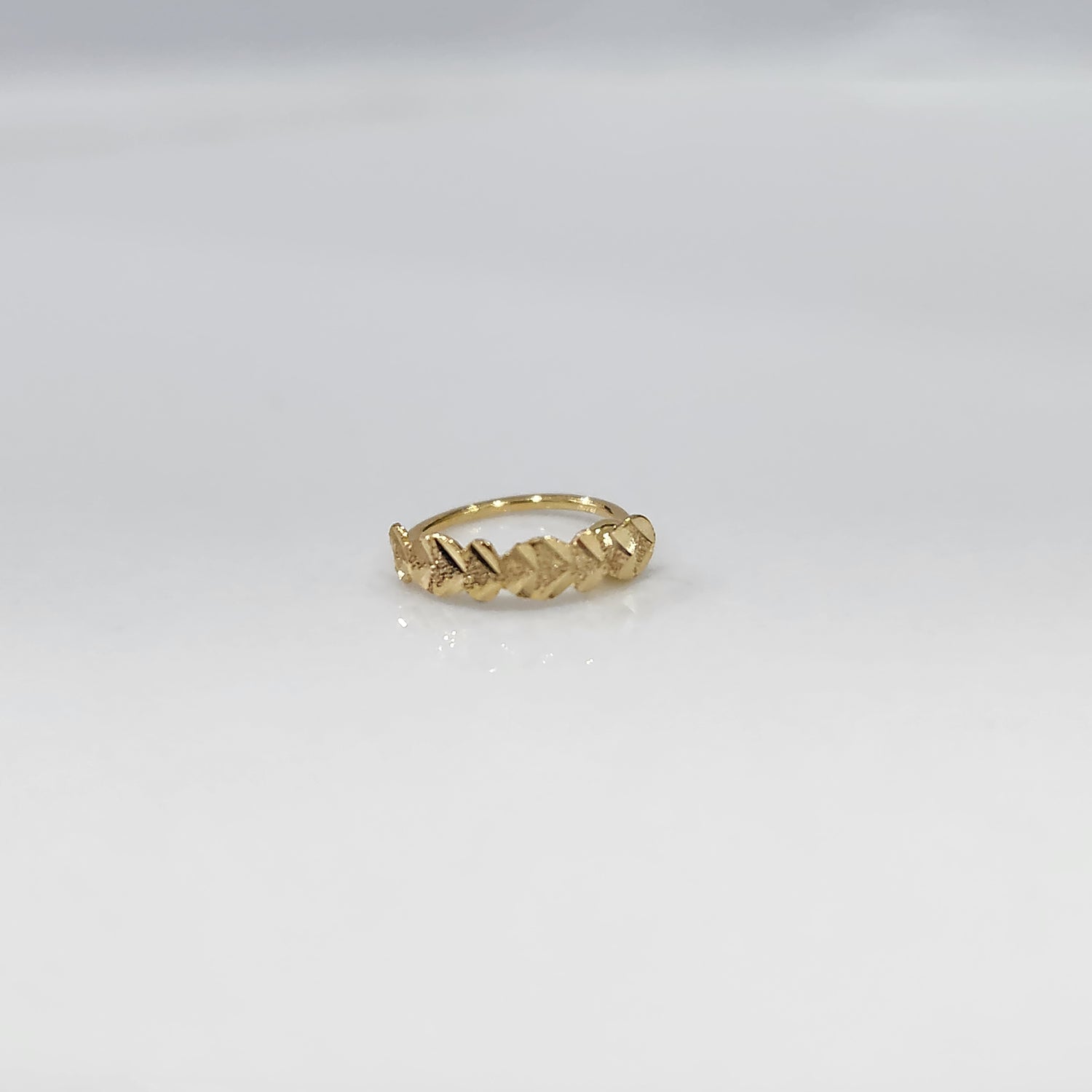 Top view of small twisted design gold nose ring placed on a clean white surface highlighting detailing