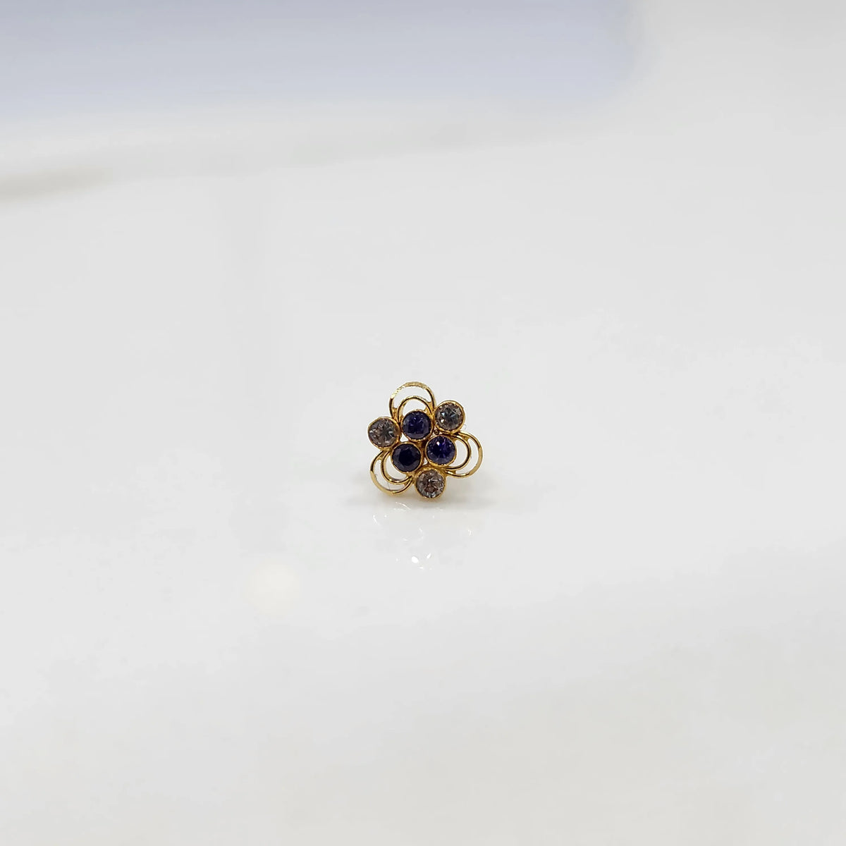Front view of a small stone gold nose pin on a white background showing the symmetrical floral setting