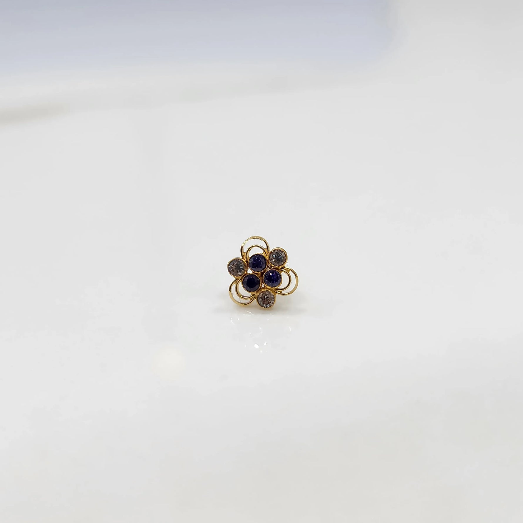 Front view of a small stone gold nose pin on a white background showing the symmetrical floral setting