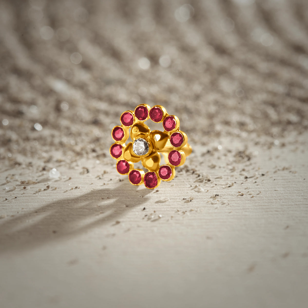 Floral gold nose pin featuring pink gemstones arranged in a flower design with a sparkling white center stone.