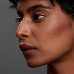 Woman wearing a tiny minimalist 18K gold nose pin shown in close side profile highlighting a natural everyday look
